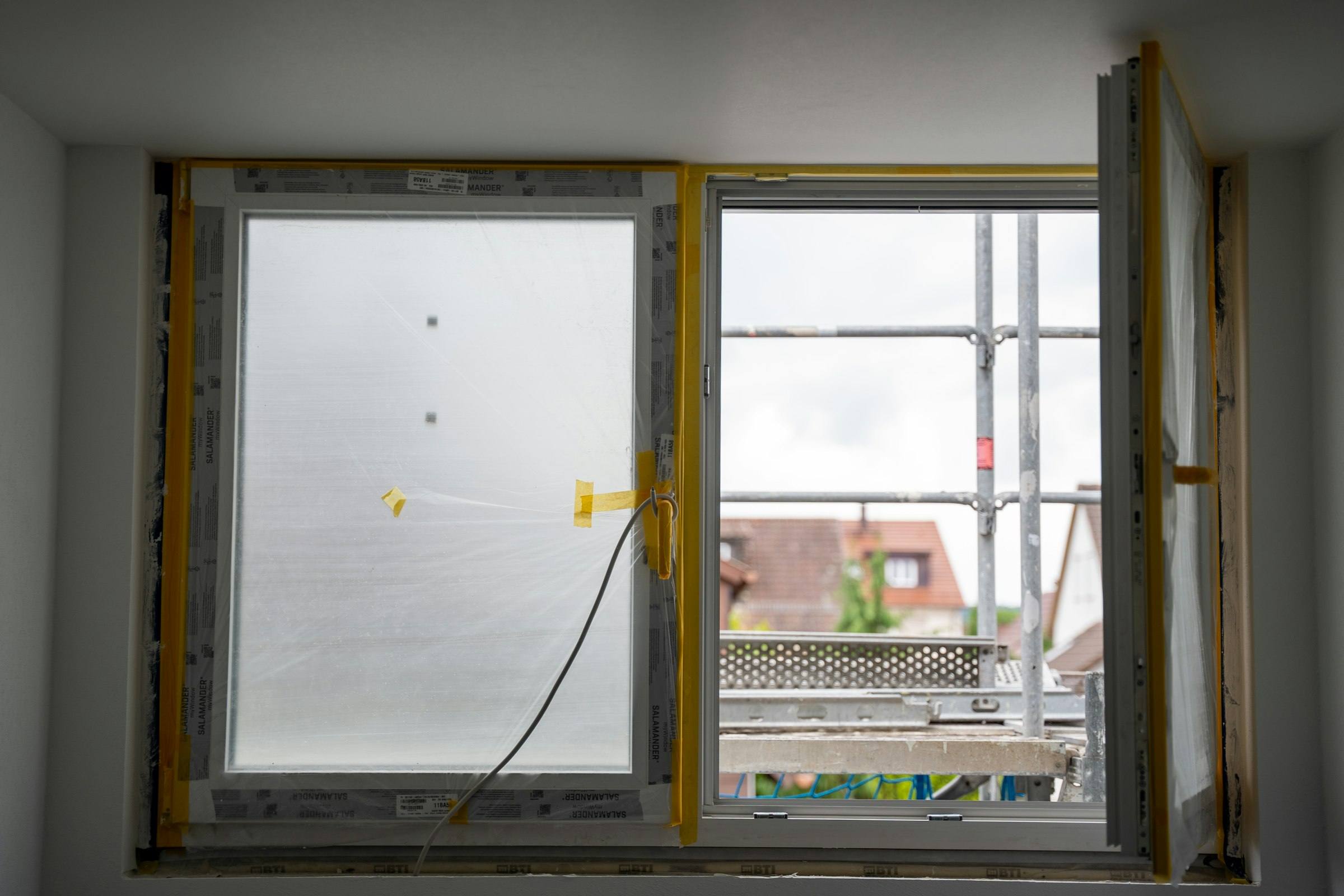 Neu eingesetztes Fenster mit gelber Abklebung und Schutzfolie, draußen ein Baugerüst